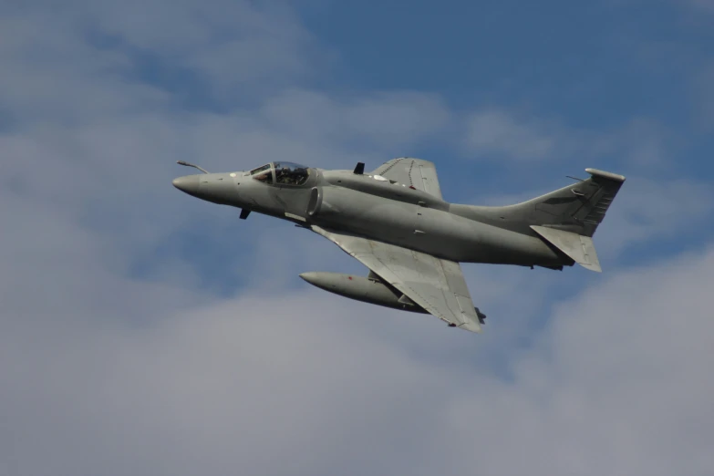 a grey jet fighter flies against the cloudy blue sky