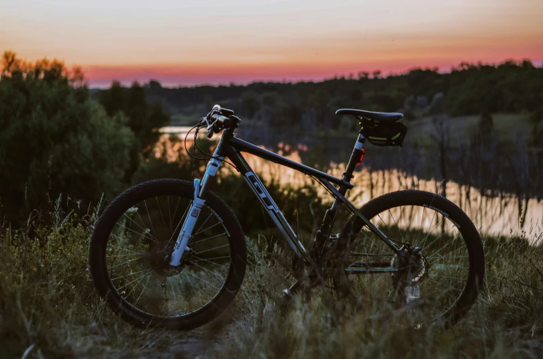 the mountain bike is parked by the water at sunset