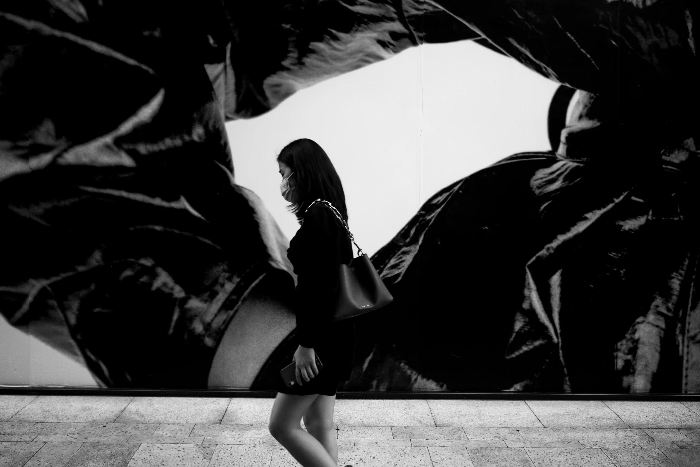 a woman standing outside of a wall with giant plant leaves on it