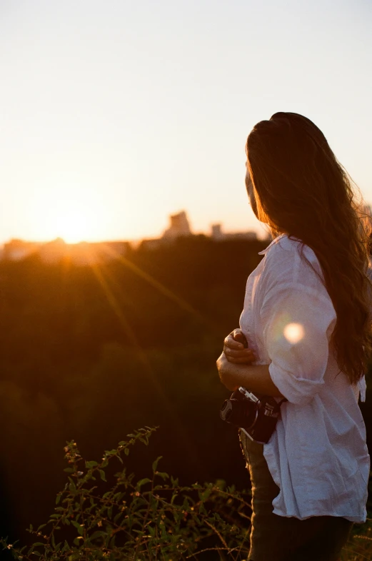 a girl standing in the sunset with the camera in her hands