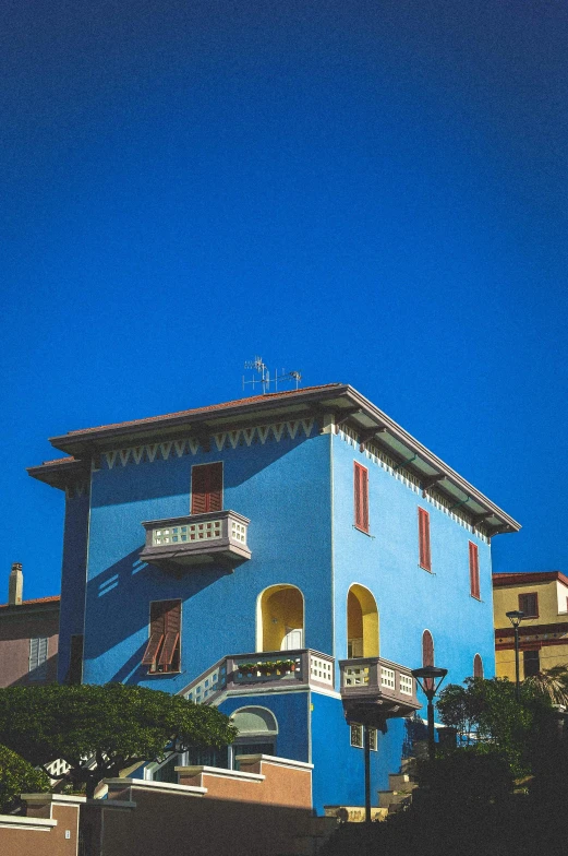 a blue building with three storyed structures and an awning, with a flag on the roof