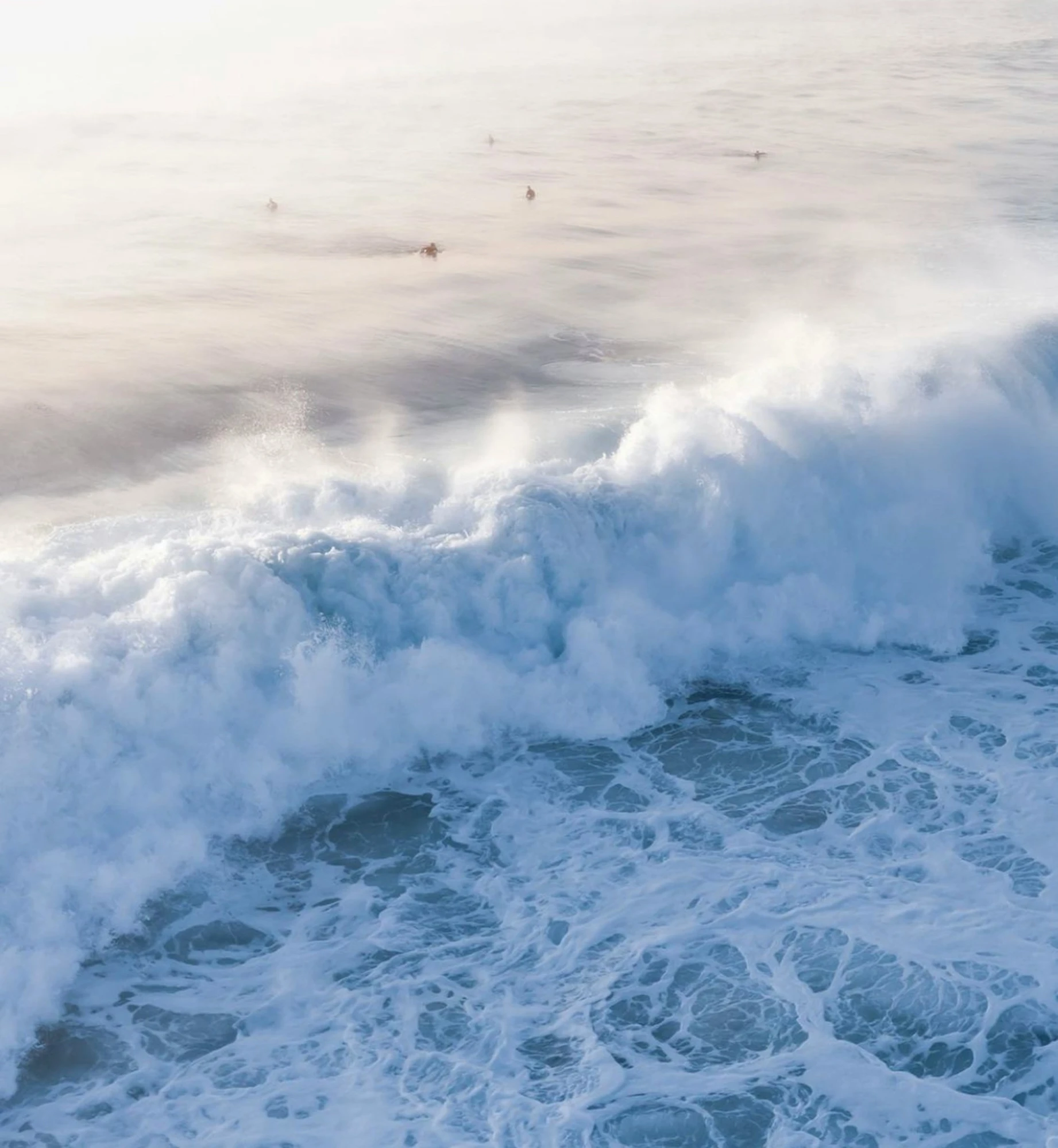 a lone surfboarders rides on the surf as strong waves crash