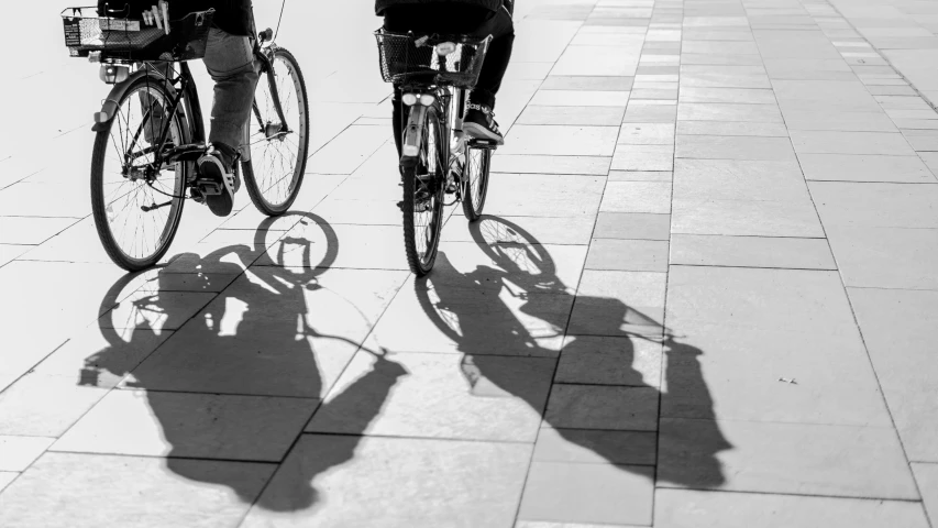 the shadow is cast on the pavement of two bikes and people standing near