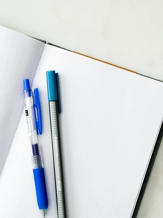 two pens and a notebook on top of a white desk