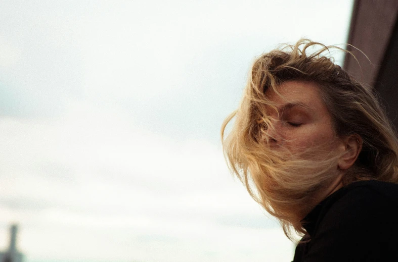 woman with long blond hair leaning against wall and looking off to the side