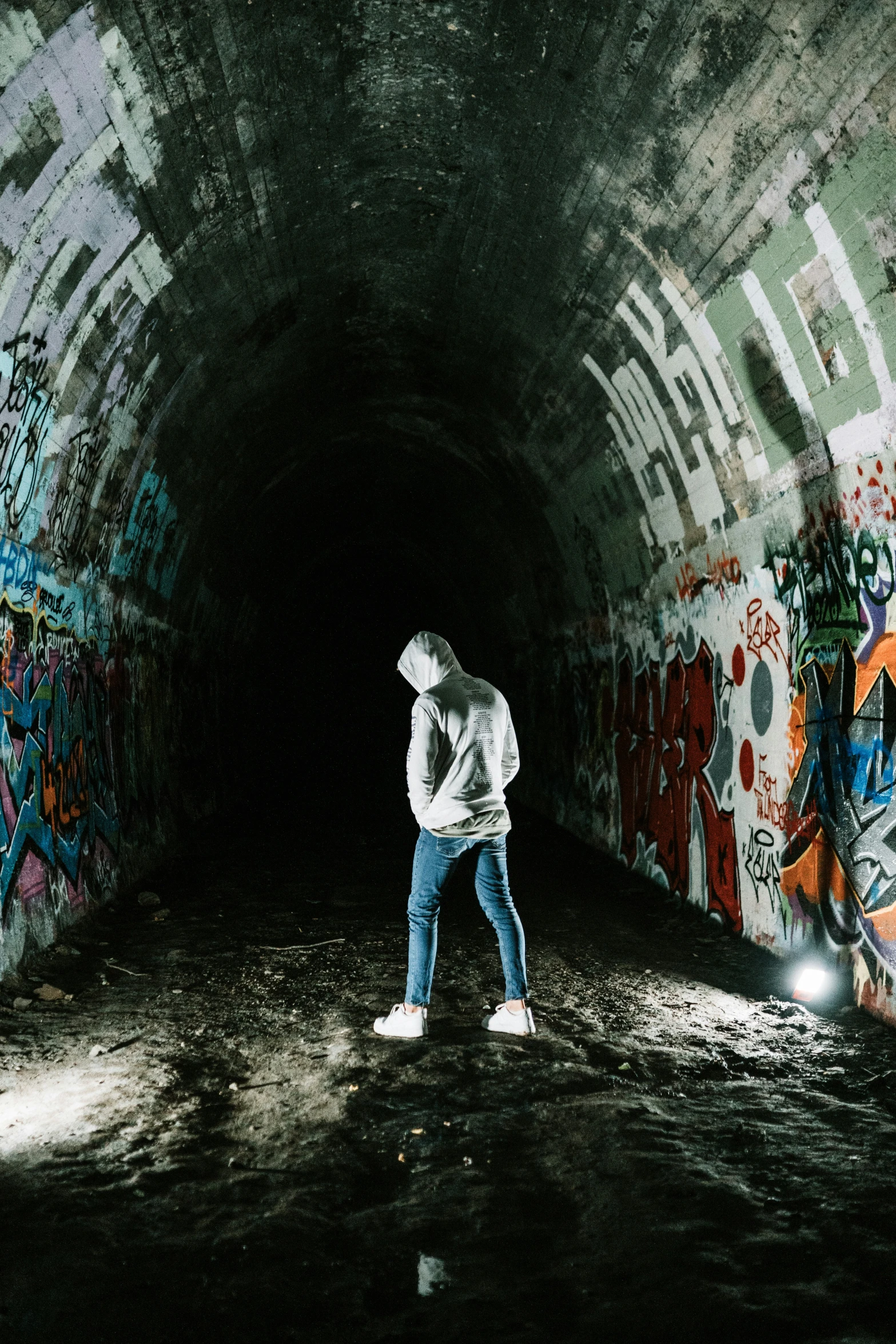 a person wearing a hat and holding an umbrella stands inside a tunnel