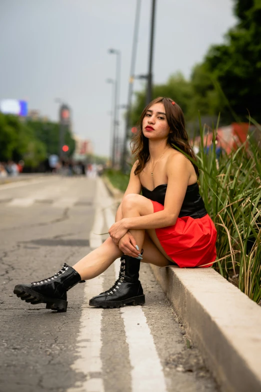 a young woman sitting down wearing boots and a red skirt