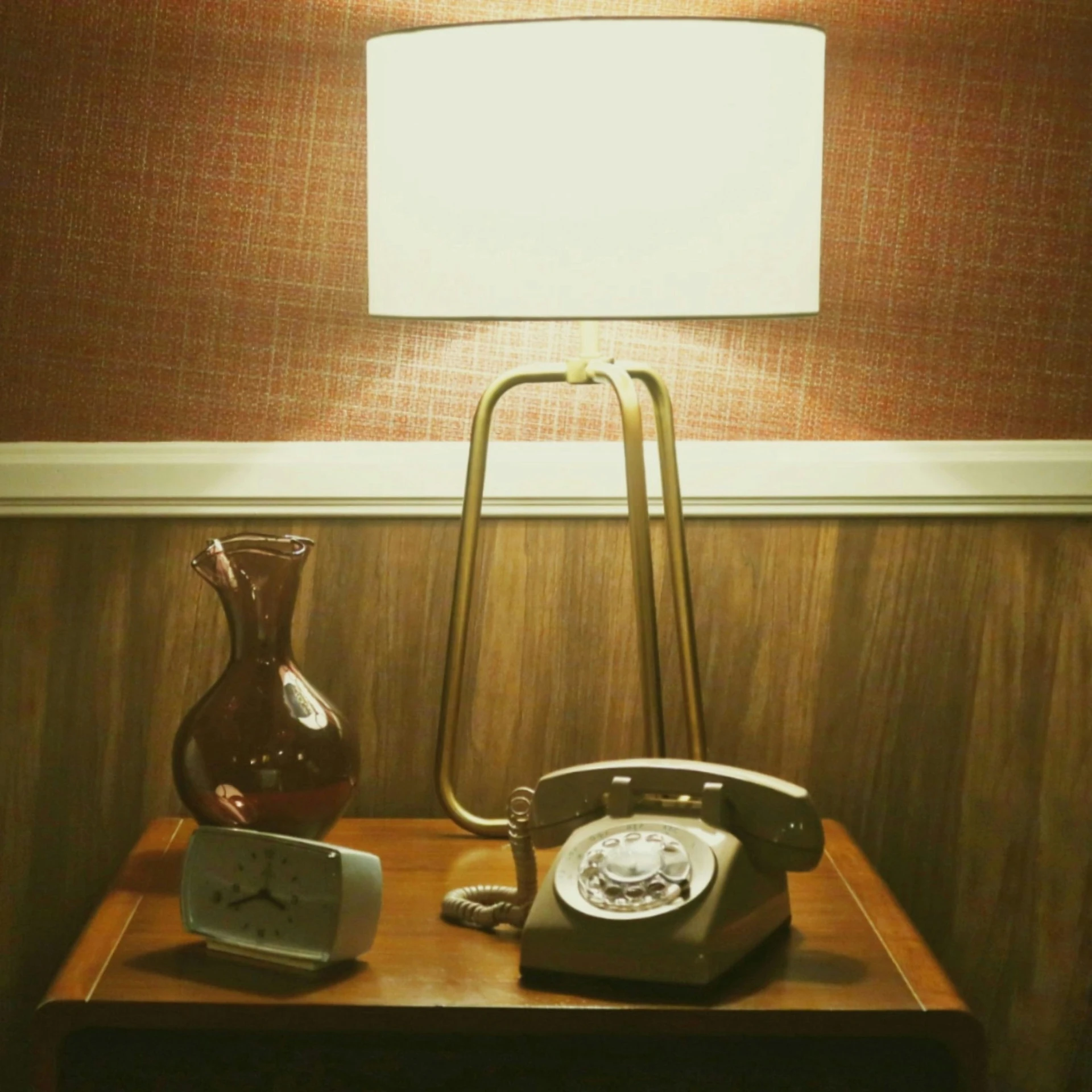 a telephone, a glass jug and an alarm clock on a table