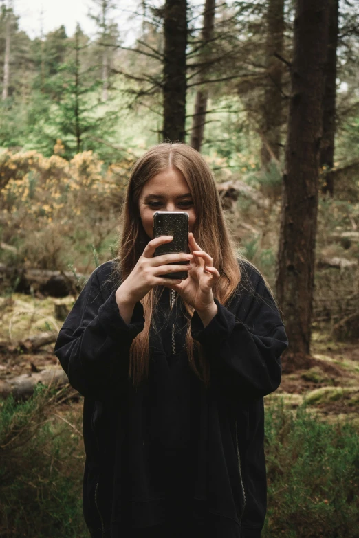 a woman standing in the woods taking a selfie