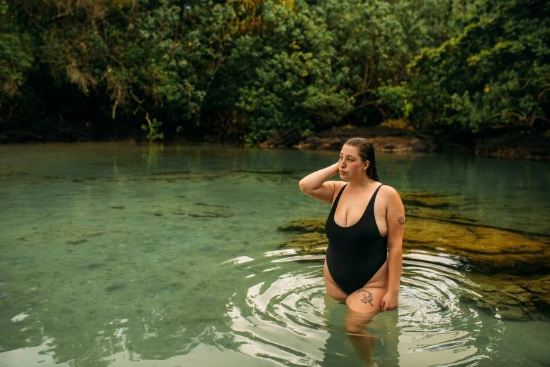 a woman in black bathing suit in water with trees