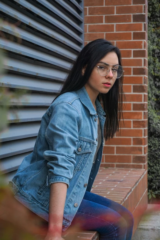 a woman in blue jean jacket and glasses on the steps of a brick building