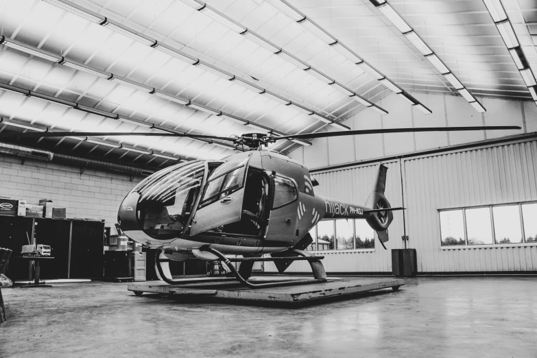 a helicopter parked in an empty hangar with equipment around it