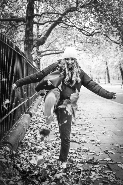 a woman standing next to a fence with leaves on the ground