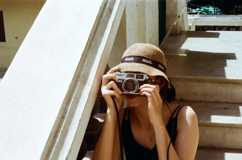 a woman in a hat with a camera next to a stair case