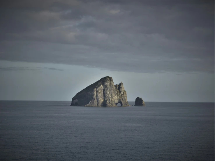 a rock formation near a calm ocean on a cloudy day