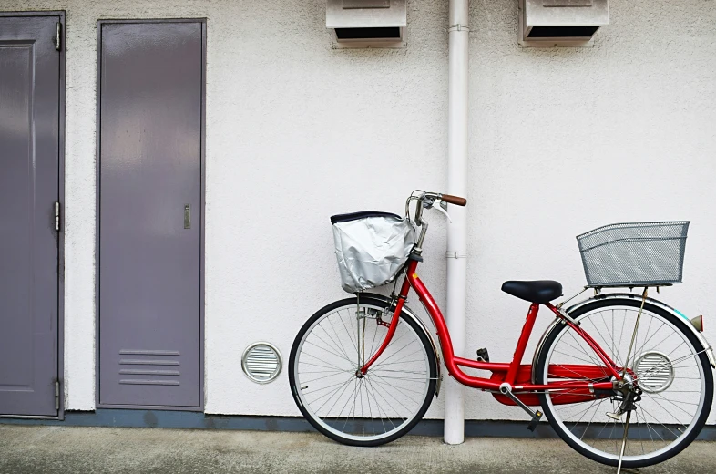 a red bike parked against a wall by a white building