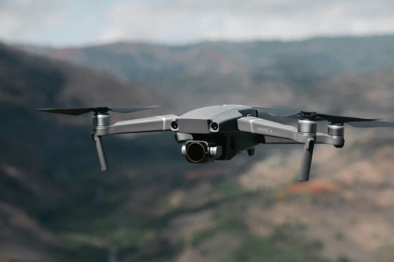 a gray remote controlled flying in front of a mountain