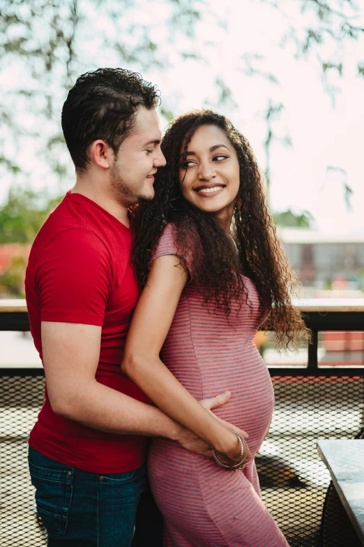 a pregnant couple cuddle together in an outdoor setting