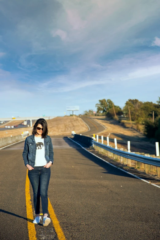 a woman is standing on the side of an empty road