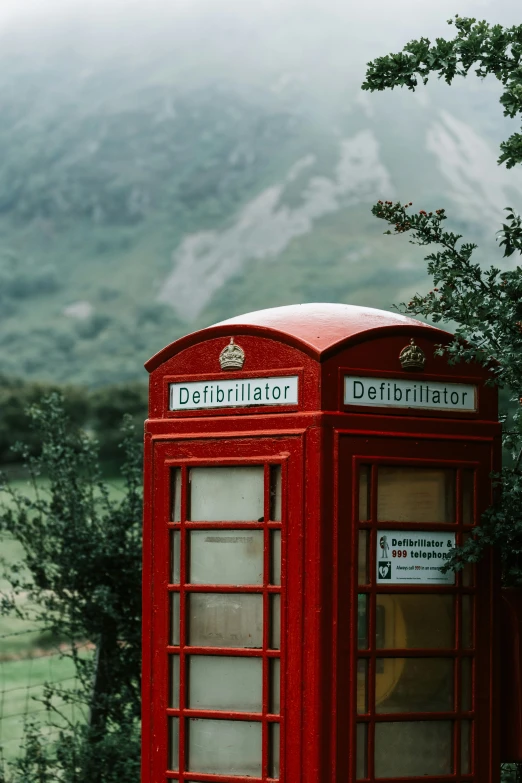an old red phone booth stands in front of a mountain range