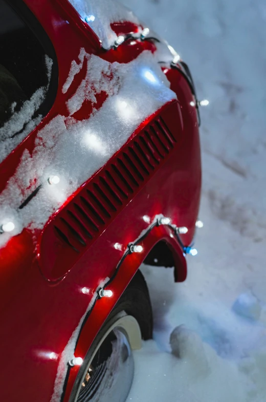 a red car with its lights on in the snow