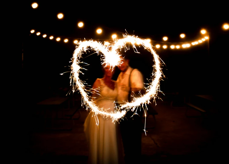 two people standing under a string light with a heart shaped star in the middle of them
