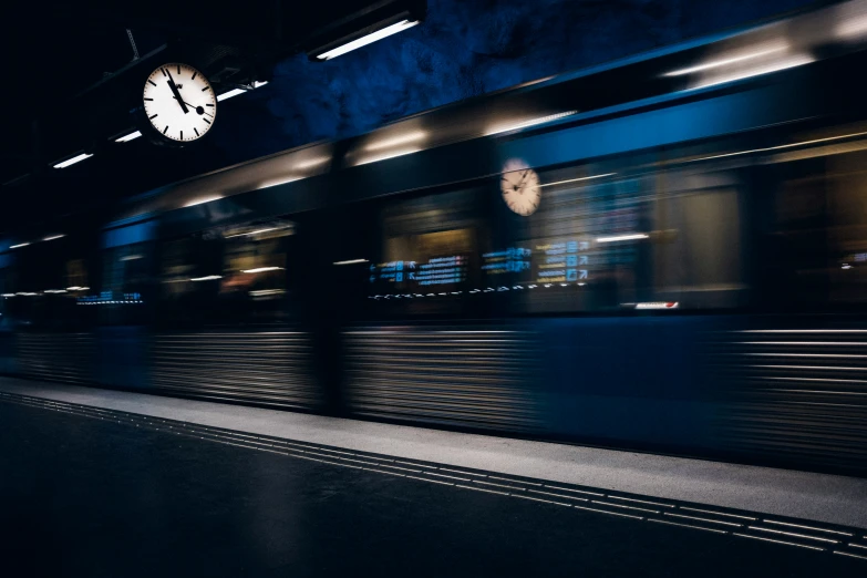 a moving train and clock at night in a train station