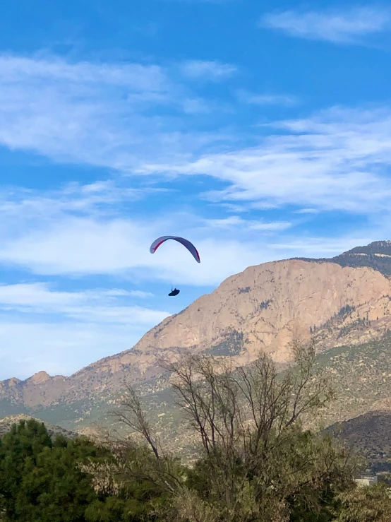 a paraglider flies in front of a mountain backdrop