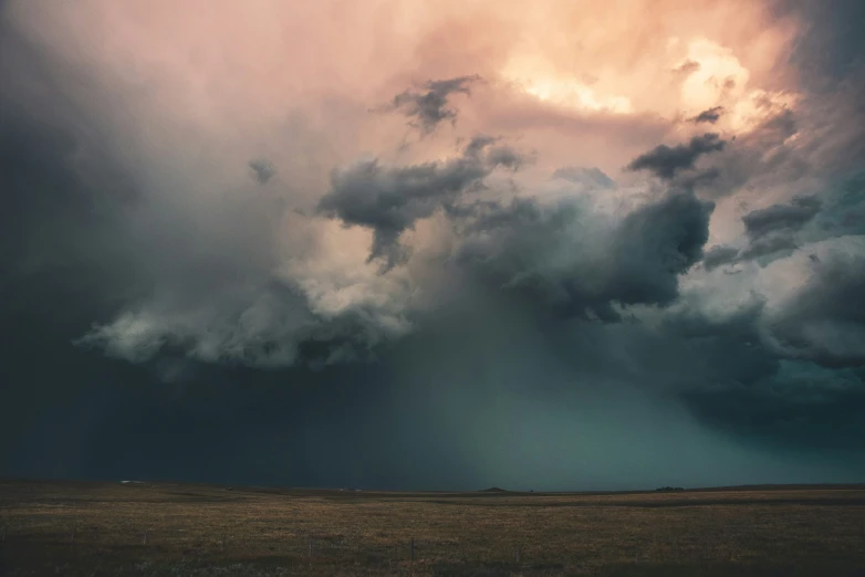 some large black clouds in the sky above some brown grass