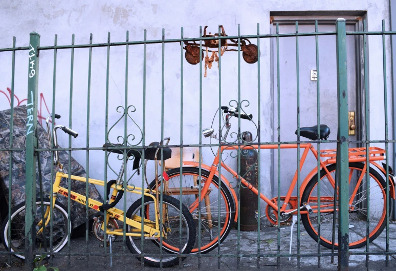an orange bike sits next to two orange bicycles behind a fence