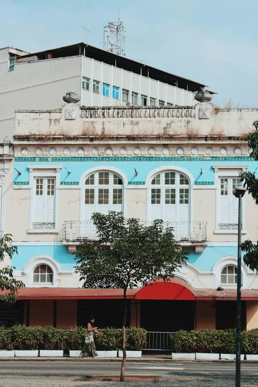 an old, blue and pink building has a bicycle rider and tree