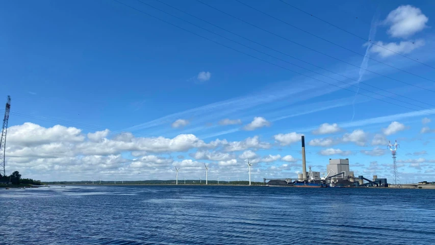 a lake with blue skies and clouds and wind farm