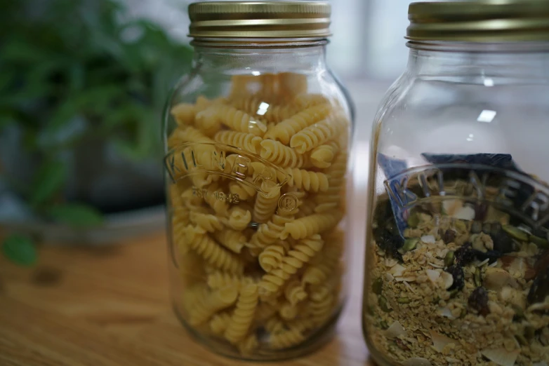 two glass jars with pasta and a plant in the background