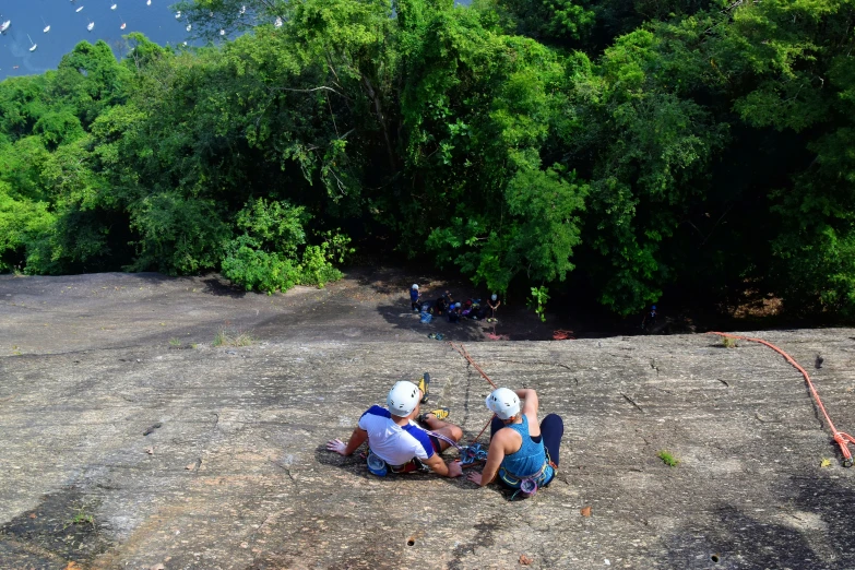 two people sit on top of a rock near some water