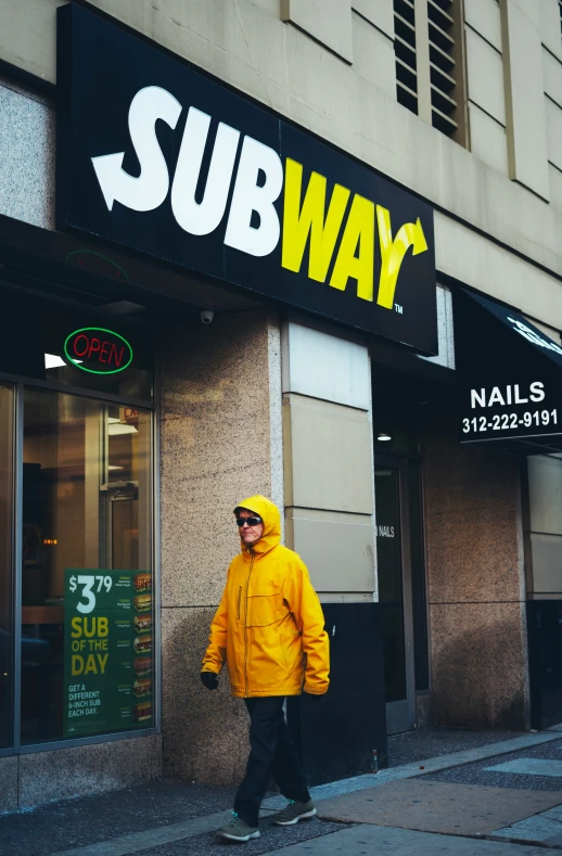 a person is walking down the sidewalk in front of a subway shop
