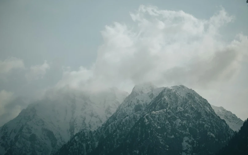 a mountain side with clouds hanging in the sky