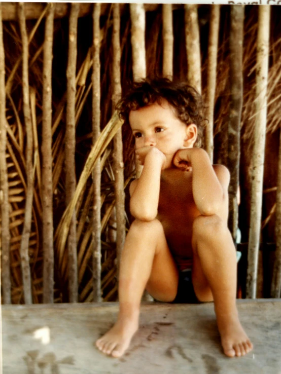 a child sitting on a wooden platform with hands on his face