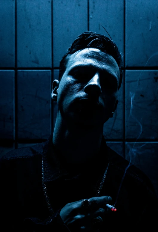 man smoking cigarette in a dark room with blue tiles