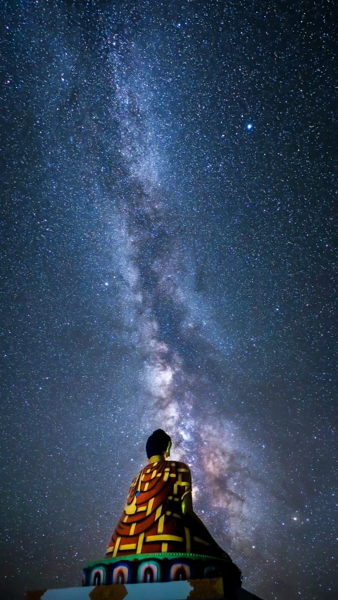 a statue in the middle of a hill that has the milky shining in the sky