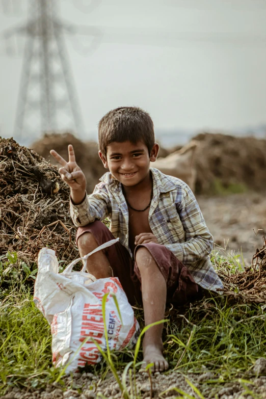 boy showing peace sign while sitting on the ground