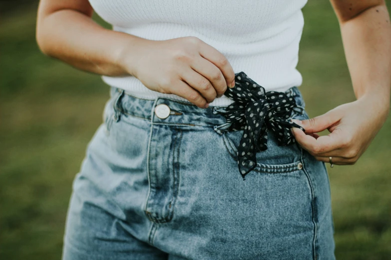 close up image of person wearing a white top and denim shorts with a black bow on the left side of their bow