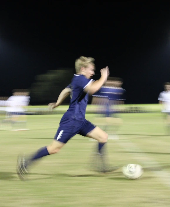 a young man playing soccer in blue uniform with ball