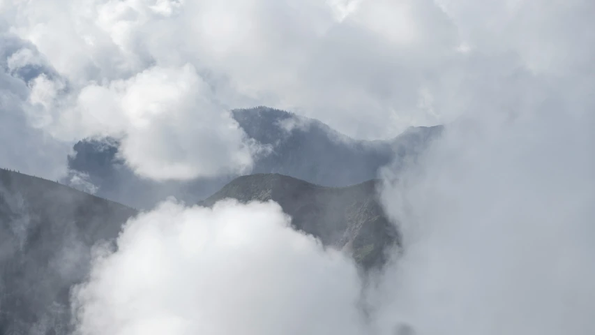 a bird flying through the clouds above a mountain