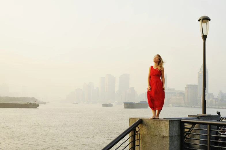 the woman is wearing a red dress standing near the harbor