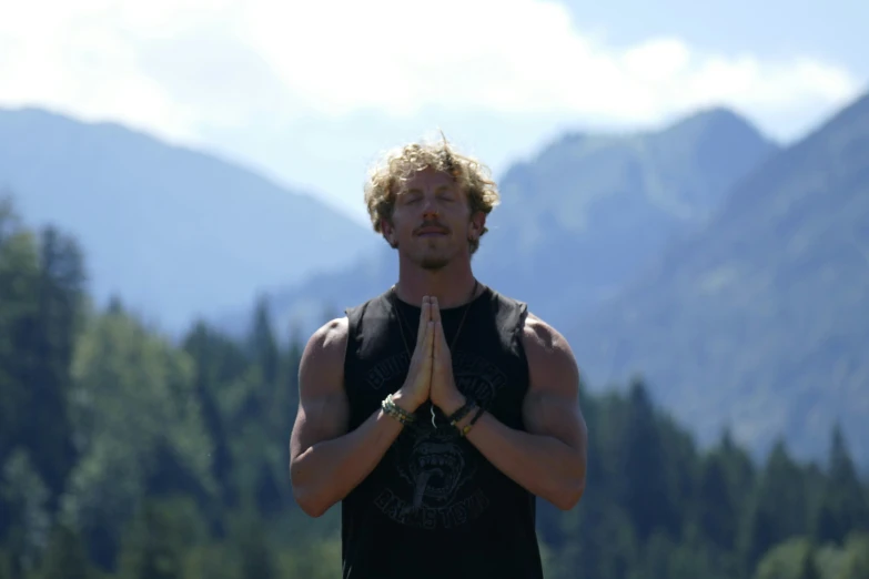 a man doing a cross - legged pose by some mountains