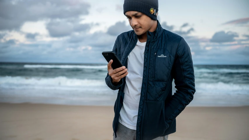 man standing on beach looking at phone wearing hat