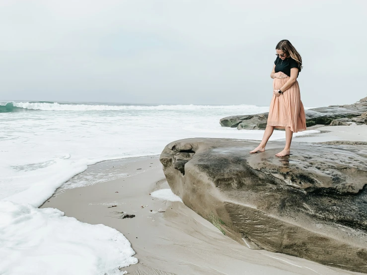 the woman is wearing a skirt and standing on a rock near the water