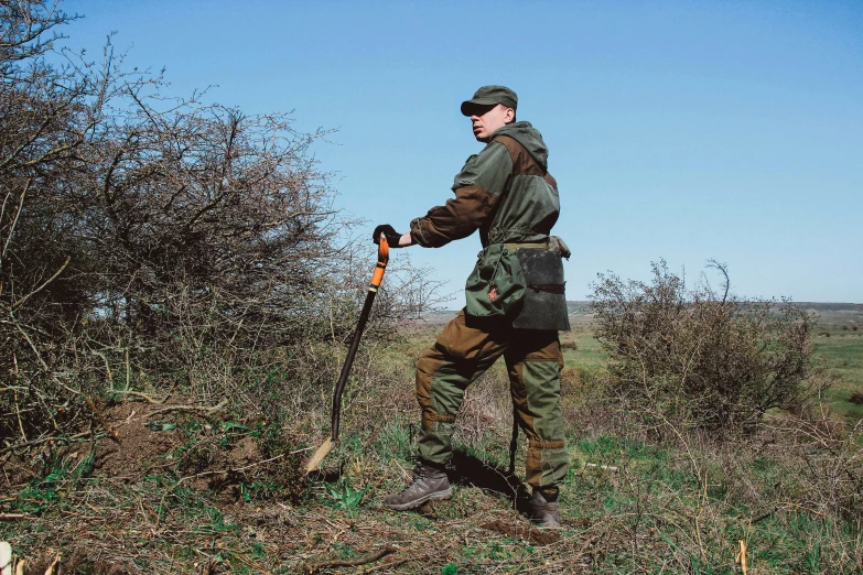 a man with an outback and hunting gear standing in the brush