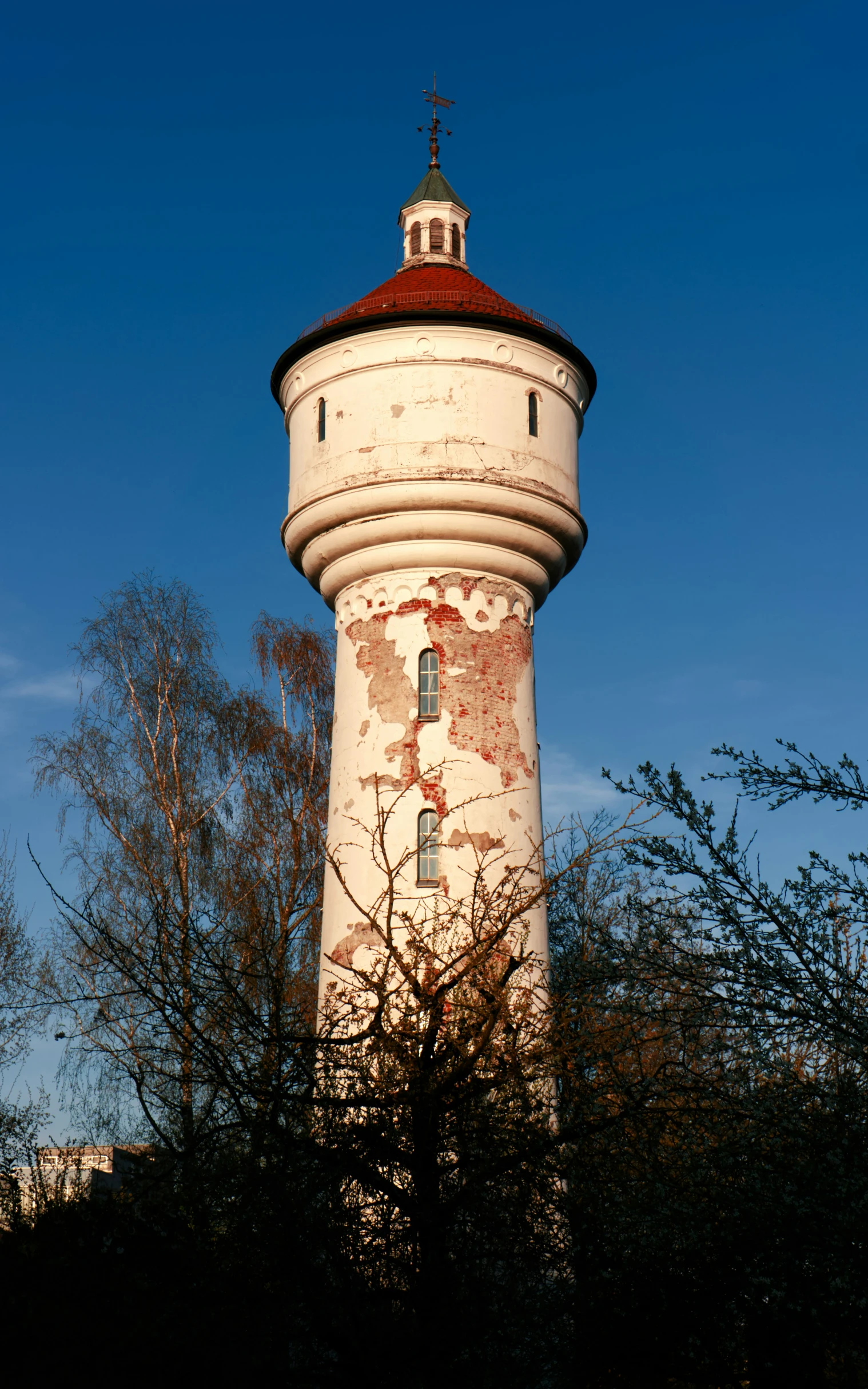 an old white and red tower with trees in front