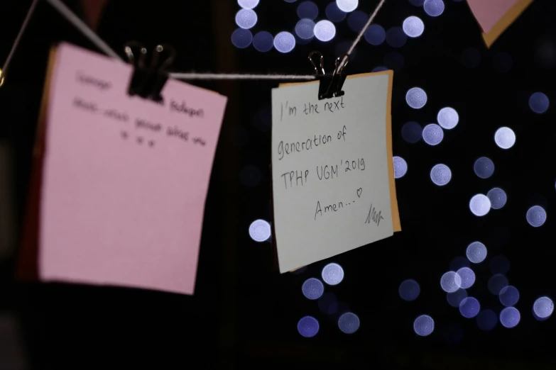 a couple of notes attached to strings with lights in the background